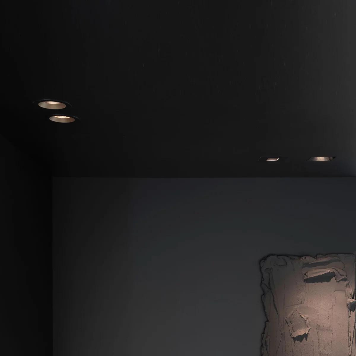 Round trimless recessed downlights set into a dark ceiling, angled to wash warm light down a pale wall onto a textured plaster relief.
